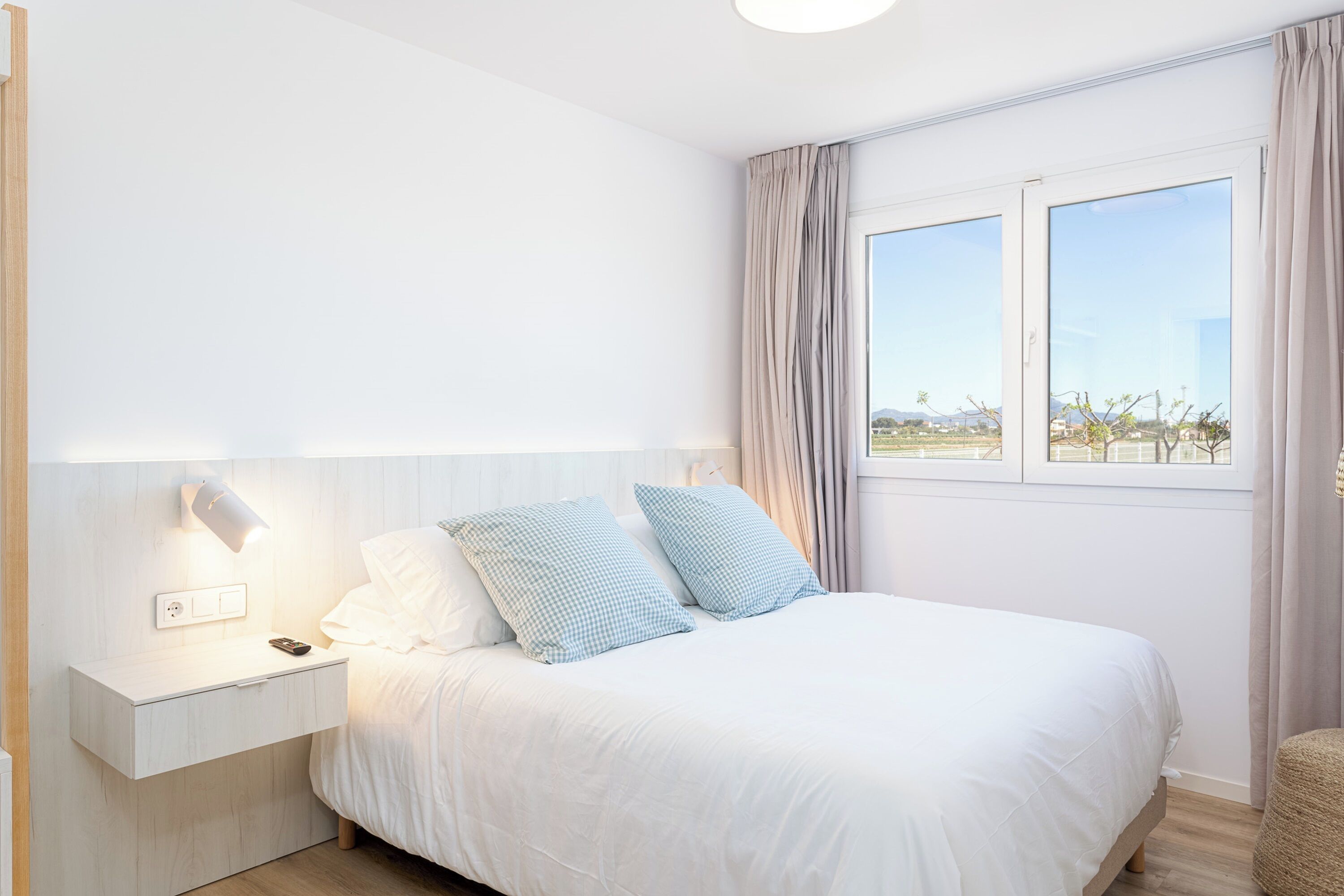 Une chambre à coucher avec un lit, une table de chevet, une lampe et une fenêtre avec des rideaux.