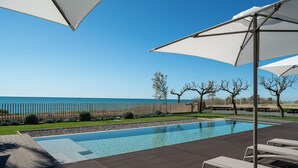 A swimming pool with lounge chairs and umbrellas, a wooden deck, and a view of the sea.