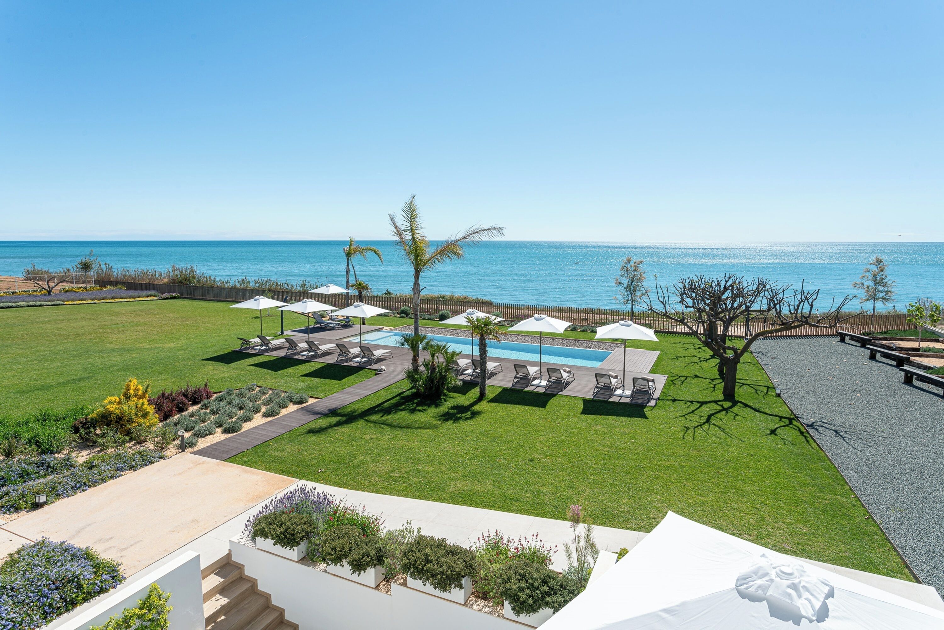 A pool area with lounge chairs and umbrellas, a well-maintained lawn, and a view of the ocean.