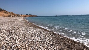 A pebbled beach with a rocky cliff and calm sea.