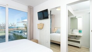 A hotel room with a large bed, a TV mounted on the wall, a bathroom with a sink and mirror, and a view of the outside.