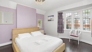 Een slaapkamer met een groot bed, een stoel, een raam met gordijnen en een schilderij aan de muur.