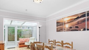Een eetruimte met een houten tafel en stoelen, een kroonluchter en uitzicht op de omgeving door een glazen deur.