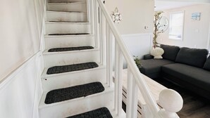 A staircase with white railings and black carpeted steps leading to a living area with a dark-colored sofa and a plant.
