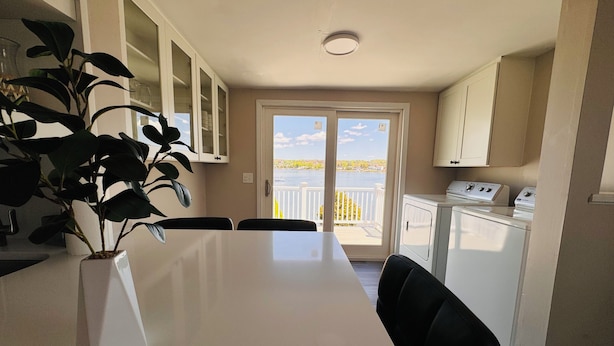A dining area with a table, chairs, a potted plant, and a view of a body of water through a glass door.