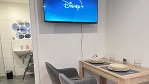 Un comedor moderno con una mesa de madera, dos sillas tapizadas en gris y un televisor de pantalla plana mostrando el logo de Disney+.