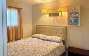 Ein Schlafzimmer mit einem gesteppten Kopfteil, einem Bett mit gemusterten Betttextilien, zwei Wandleuchten, einem Poster und einem kleinen Nachttisch.