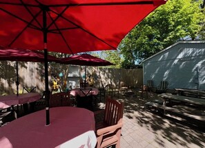 Eine Außenpatio mit Tischen und Stühlen, überdacht mit roten Sonnenschirmen, und ein Holzzaun im Hintergrund.