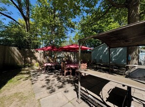 Eine Terrasse im Freien mit Tischen und Stühlen, überdacht mit roten Sonnenschirmen, und ein überdachter Sitzbereich.