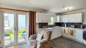 A modern kitchen with white cabinets, a built-in oven, and a dining area with a chair and table.