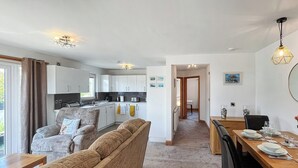 A modern living room with a sofa, a dining table set for two, and a kitchen in the background.