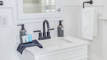 A bathroom with a white sink, black faucet, and soap dispensers. There are three bottles of lotion on the sink.