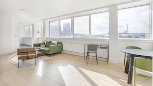 Un salón amplio con un gran ventanal, un sofá verde, una mesa de comedor y una silla.