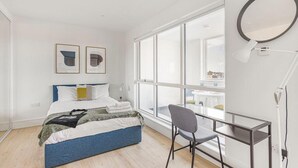 Un dormitorio moderno con cama, escritorio y ventanas amplias.