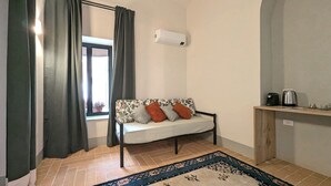 A cozy room with a sofa, a patterned rug, a window with curtains, and a coffee maker on a shelf. - La Corte dei Panni (Rome)