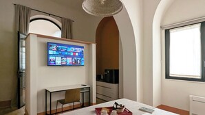 A hotel room with a bed, a desk, a TV mounted on the wall, a window, and a chandelier. - La Corte dei Panni (Rome)