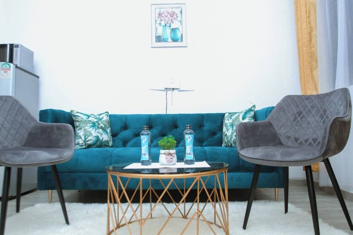 Una sala de estar con un sofá color turquesa, dos sillones grises, una mesita de centro redonda y una alfombra blanca.
