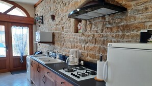 Una cocina con pared de piedra, armarios de madera, estufa a gas, cafetera y refrigerador.