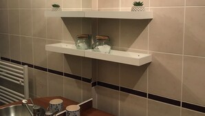 Un baño con un lavamanos de acero inoxidable, un espejo y dos estantes con frascos y una planta pequeña.
