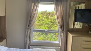 A bedroom with a bed, a window with curtains, a radiator, a TV, and a dresser. - Luxury Rural Hottub Lodge in Northumberland (Morpeth)