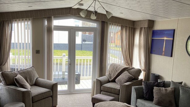 A spacious living room with a large sliding glass door leading to a balcony, grey sofas, and a modern ceiling design. - Luxury Rural Hottub Lodge in Northumberland (Morpeth)