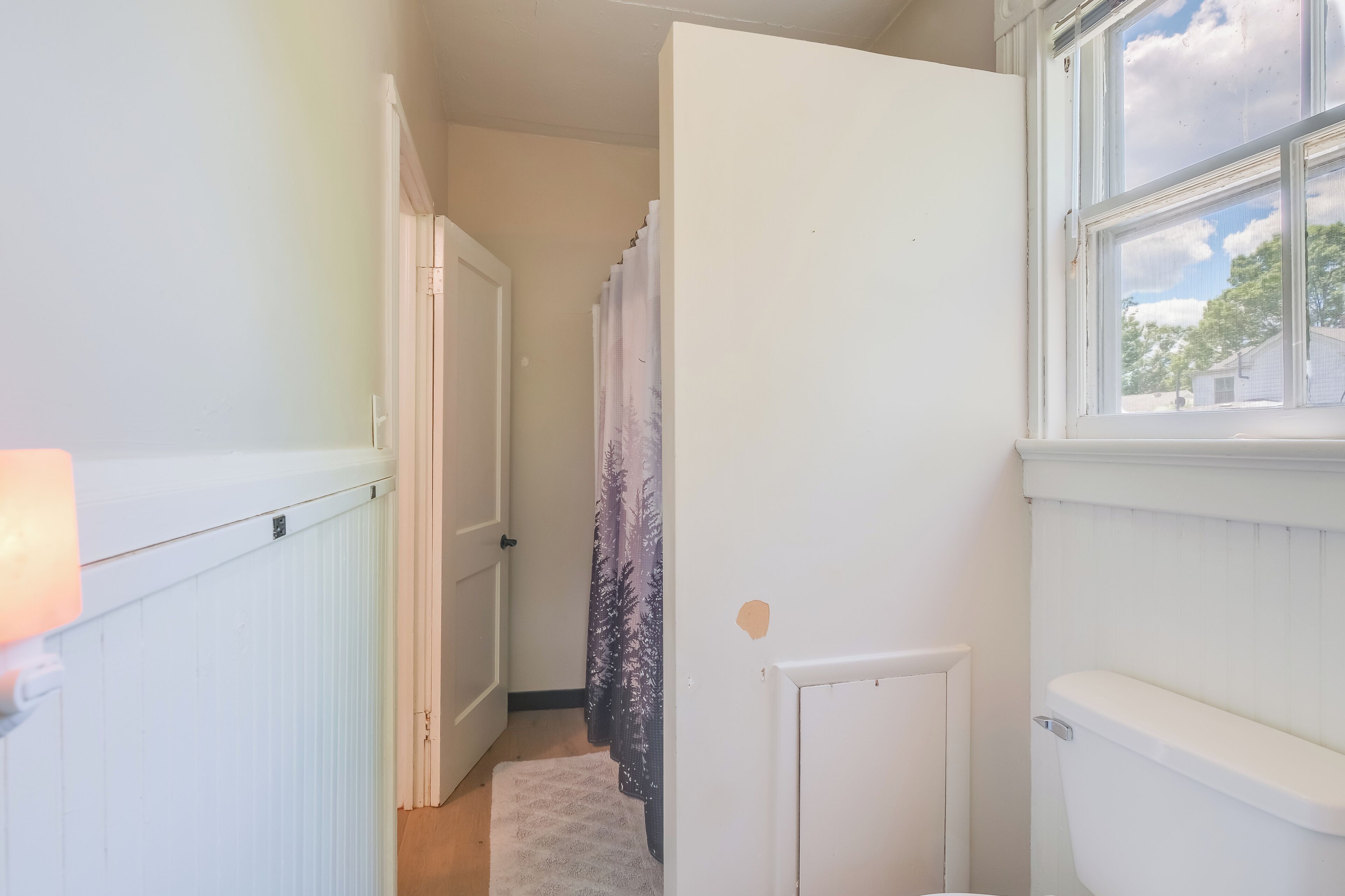 A narrow hallway with a white radiator, a door, and a window with a view of trees and a house.