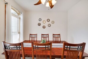 Una sala da pranzo con un tavolo in legno e sei sedie, una ventola a soffitto e decorazioni a parete.