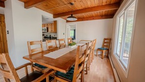 Een eethoek met een houten tafel en stoelen, een plafondventilator en zicht op de keuken in de achtergrond.