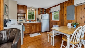 A compact kitchen with wooden cabinets, a white refrigerator, a stove, and a dining table with chairs.