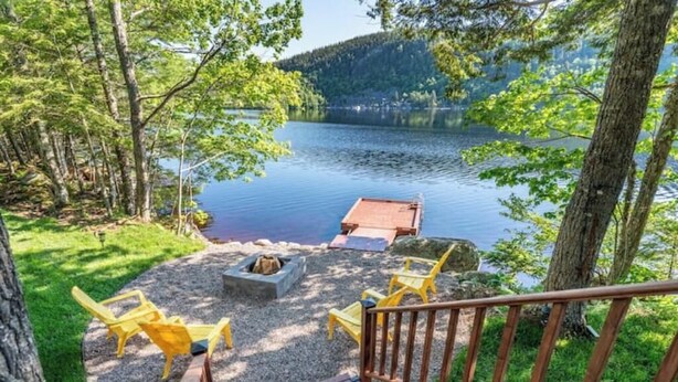 A deck with a fire pit and yellow chairs overlooking a lake surrounded by trees. - Lakeside Guest House - Porters Lake (Porters Lake)