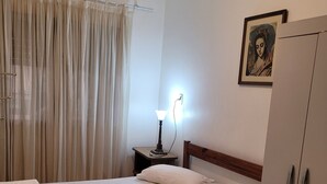 Ein ordentlich bezogenes Bett mit weißer Bettdecke und Kissen, eine Nachttischlampe, ein Holz-Kopfteil, ein Kleiderschrank und ein gerahmtes Bild an der Wand.