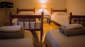 Ein Hotelzimmer mit drei hölzernen Betten, einem Nachttisch und einer Lampe.