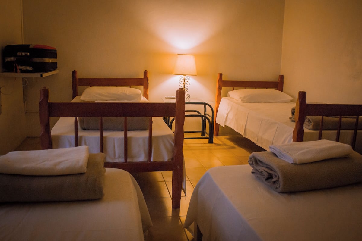 Une chambre d’hôtel avec trois lits en bois, une table de chevet et une lampe.