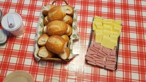 Ein Tisch mit einer rot-weißen Karomustertischdecke, einem Brötchenkorb, einer Käseplatte und einer Wurstplatte.