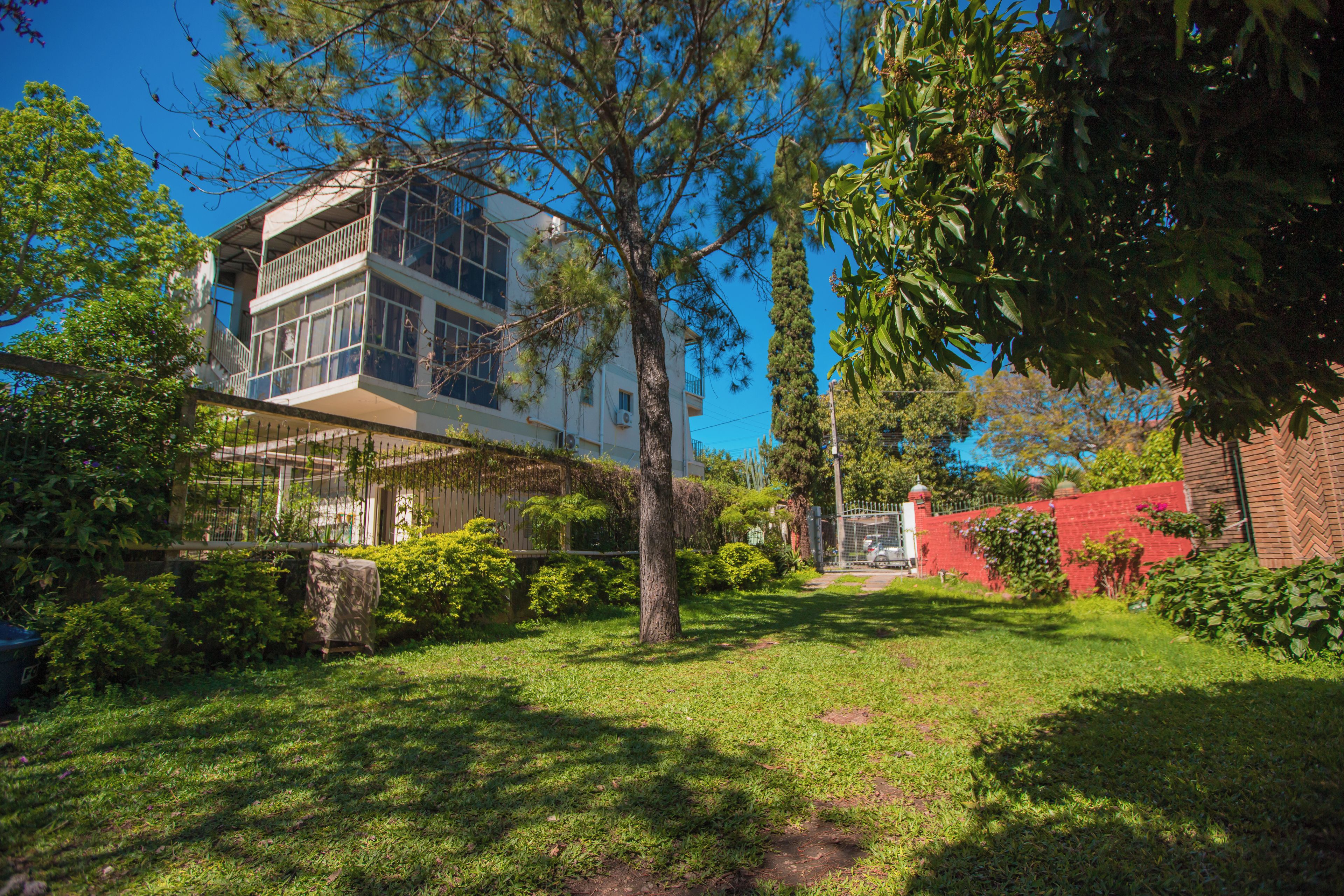 A residential building with a balcony, surrounded by greenery and a clear sky.