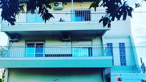 Ein zweistöckiges Gebäude mit einem Balkon im oberen Geschoss. Vor dem Haus sind zwei Autos geparkt, eines weiß und eines kastanienbraun.