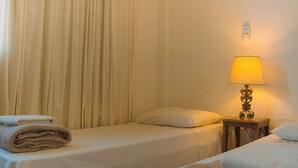 Ein Hotelzimmer mit zwei Betten, einem Nachttisch mit Lampe und einem an der Wand montierten Thermostat.