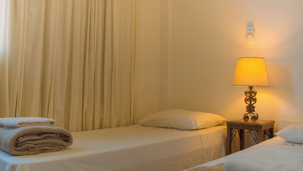 Ein Hotelzimmer mit zwei Betten, einem Nachttisch mit Lampe und einem an der Wand montierten Thermostat.