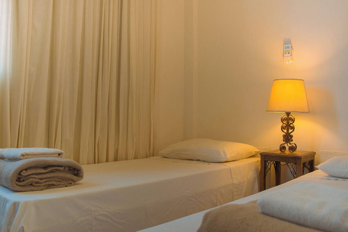 Une chambre d’hôtel avec deux lits, une table de chevet avec une lampe et un thermostat fixé au mur.
