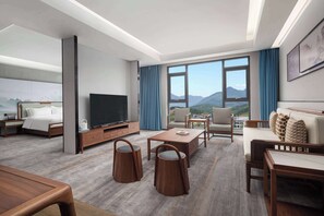 A modern hotel room with a large bed, a flat-screen TV, a sofa, a coffee table, and a view of mountains through large windows. - Days Inn by Wyndham Pingxiang Wugong Mountain (Pingxiang)