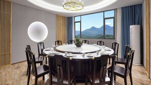 Una mesa de comedor redonda con sillas, una araña y vistas a montañas a través de amplios ventanales.