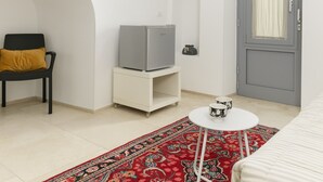 A compact room with a bed, a small table with two cups, a television on a stand, a chair with a cushion, a door, and a patterned rug. - Bianca Fortezza by Wonderful Italy (Ostuni)