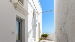 A narrow alleyway with a white building, a door, and a potted plant on a stone ledge. - Bianca Fortezza by Wonderful Italy (Ostuni)
