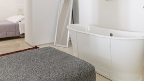 A modern bedroom with a large bathtub, a painting on the wall, and a bed with a view through an archway. - Bianca Fortezza by Wonderful Italy (Ostuni)