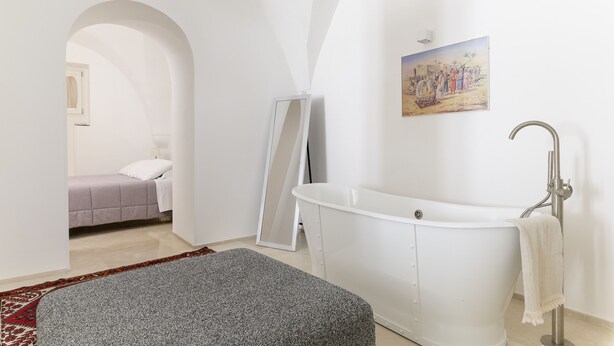 A modern bathroom with a freestanding bathtub, a large mirror, and a painting on the wall. - Bianca Fortezza by Wonderful Italy (Ostuni)