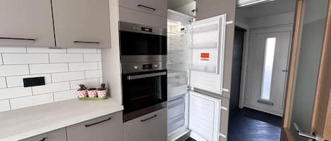 A modern kitchen with a built-in oven, a double-door refrigerator, and a countertop with potted plants.