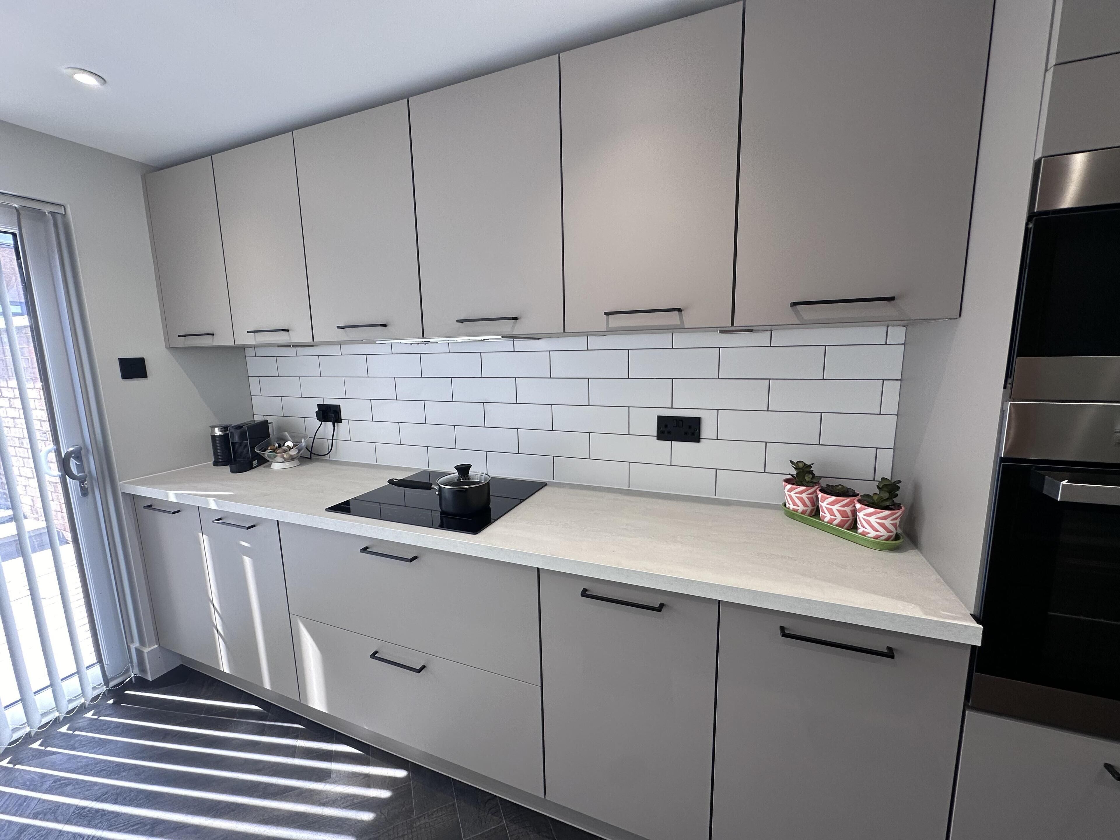 A modern kitchen with grey cabinets, a white tiled backsplash, and a black induction cooktop.