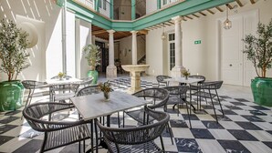 Een ruime binnentuin met zwart-witte vloertegels, meerdere tafels en stoelen, en potplanten.