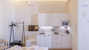 Een kleine hotelkamer met een bed, nachtkastje en een kitchenette.