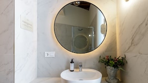 Een badkamer met een ronde spiegel, een wit wastafelmeubel en een potplant.